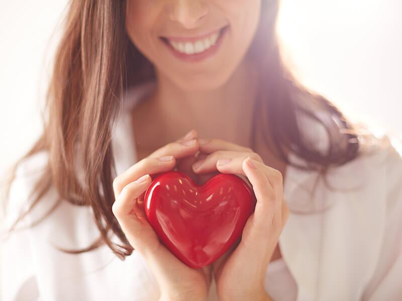 femme souriante tenant un coeur rouge dans les mains