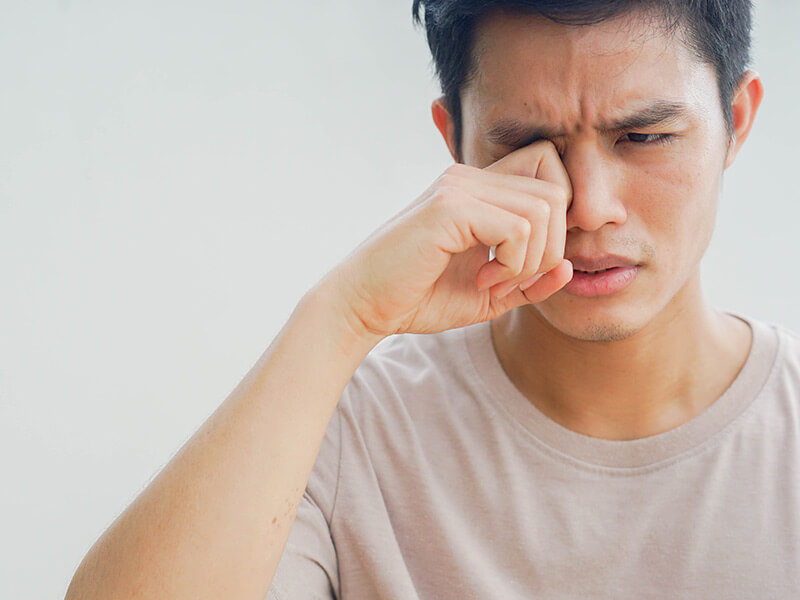 jeune homme se frottant l'œil avec un air de douleur