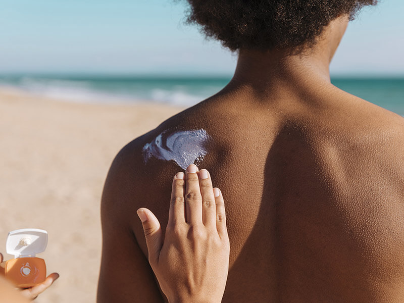 femme appliquant de la crème solaire sur le dos d'un jeune homme